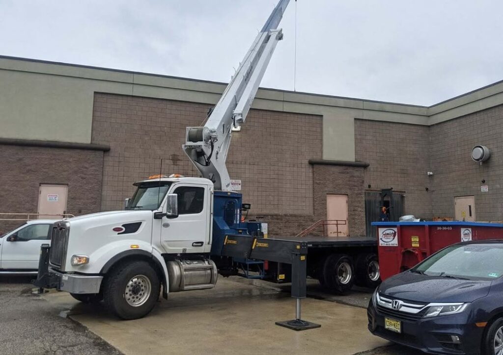 Boom truck for material handling services. White crane truck with outriggers extended, parked near a commercial building. Material delivery in Boston, MA.