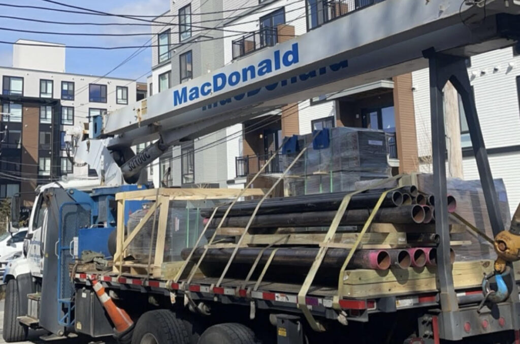 Boom truck carrying pipes and materials in Boston, MA. Choosing between a 30-ton boom truck or a 50-ton crane?
